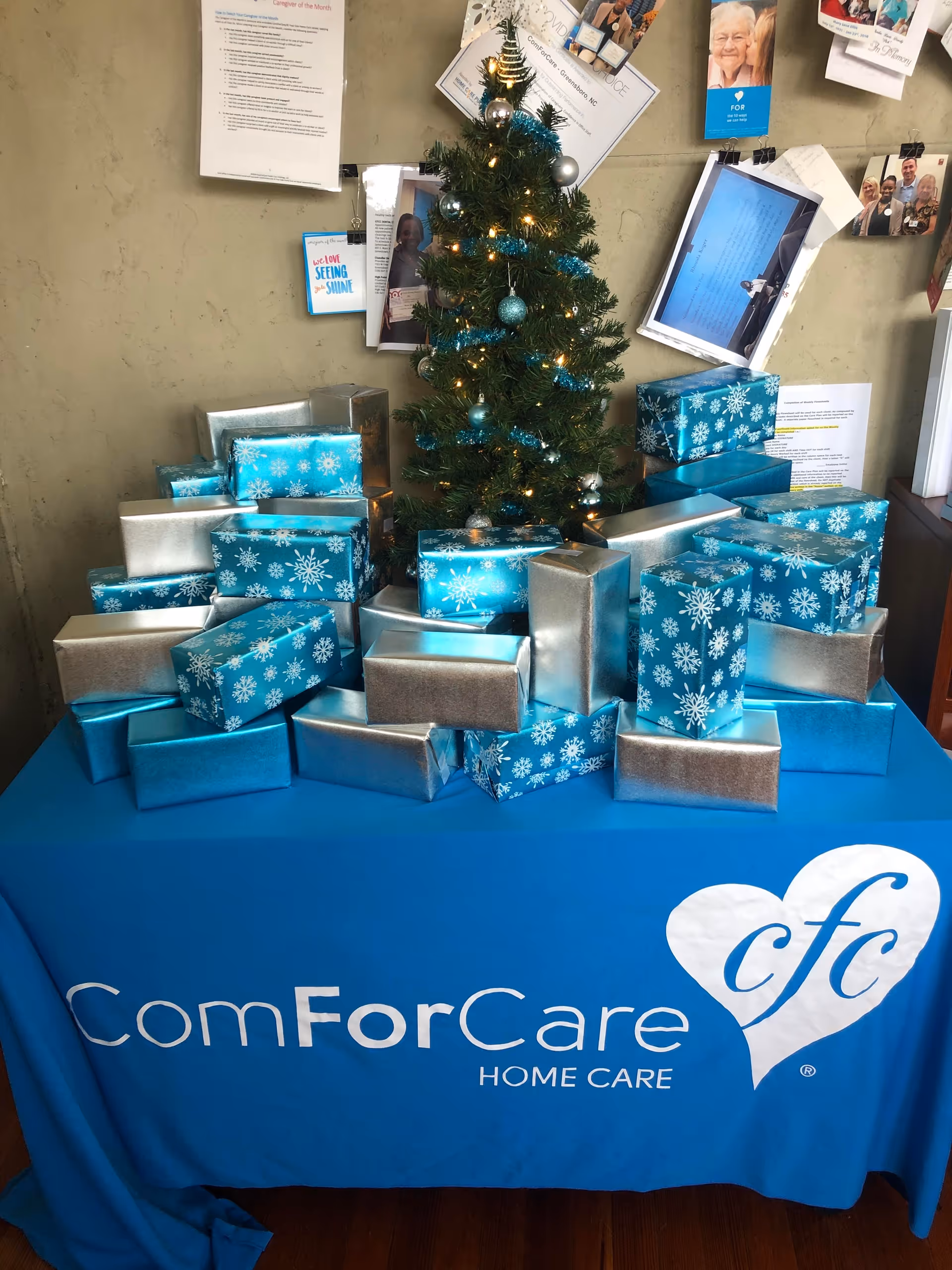 Decorated indoor display with a Christmas tree and many wrapped gifts on a ComForCare table