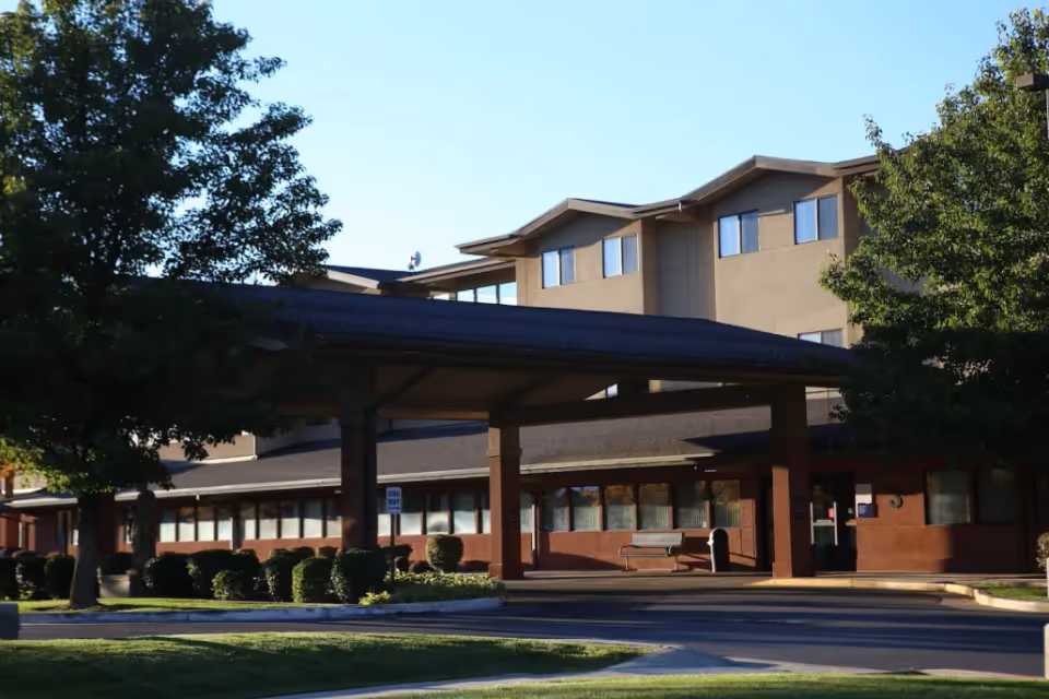 Covered entrance and porte-cochère of a multi-story senior living building with trees and landscaping.