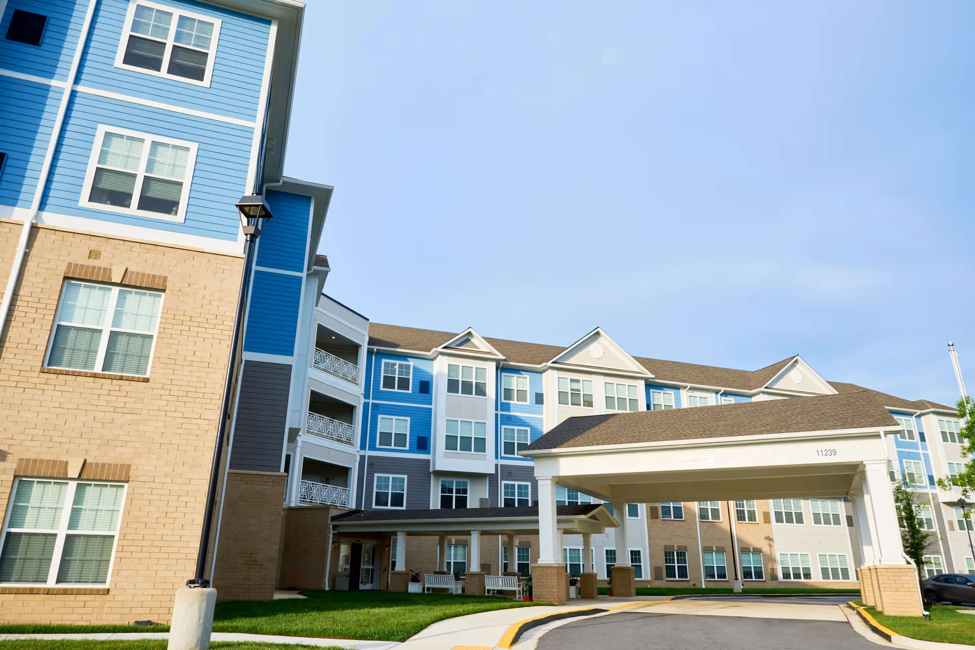 Blue and beige senior living building with a covered entrance and balconies under a clear sky.
