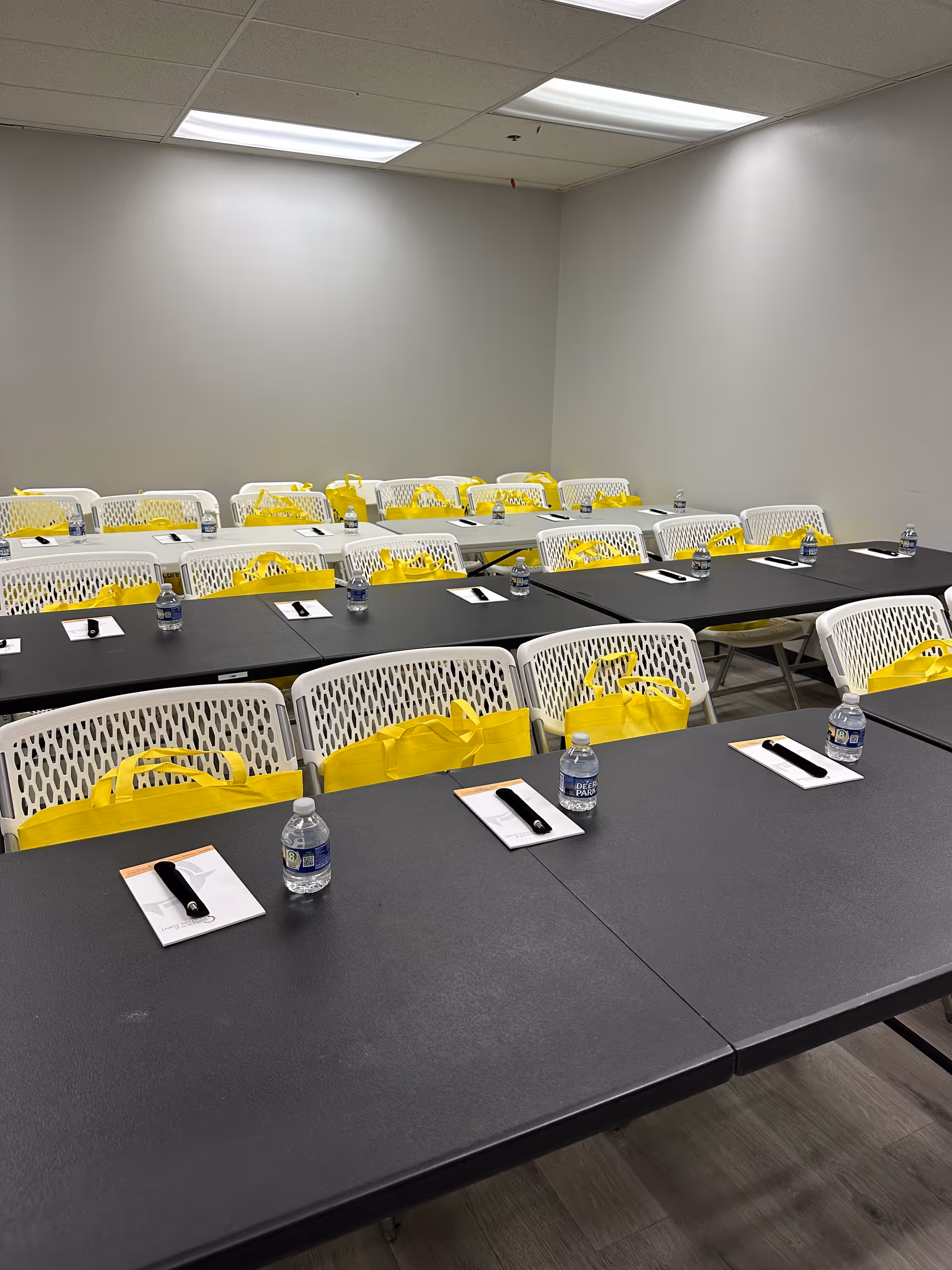 Large classroom setup with black tables, white chairs, and yellow bags.