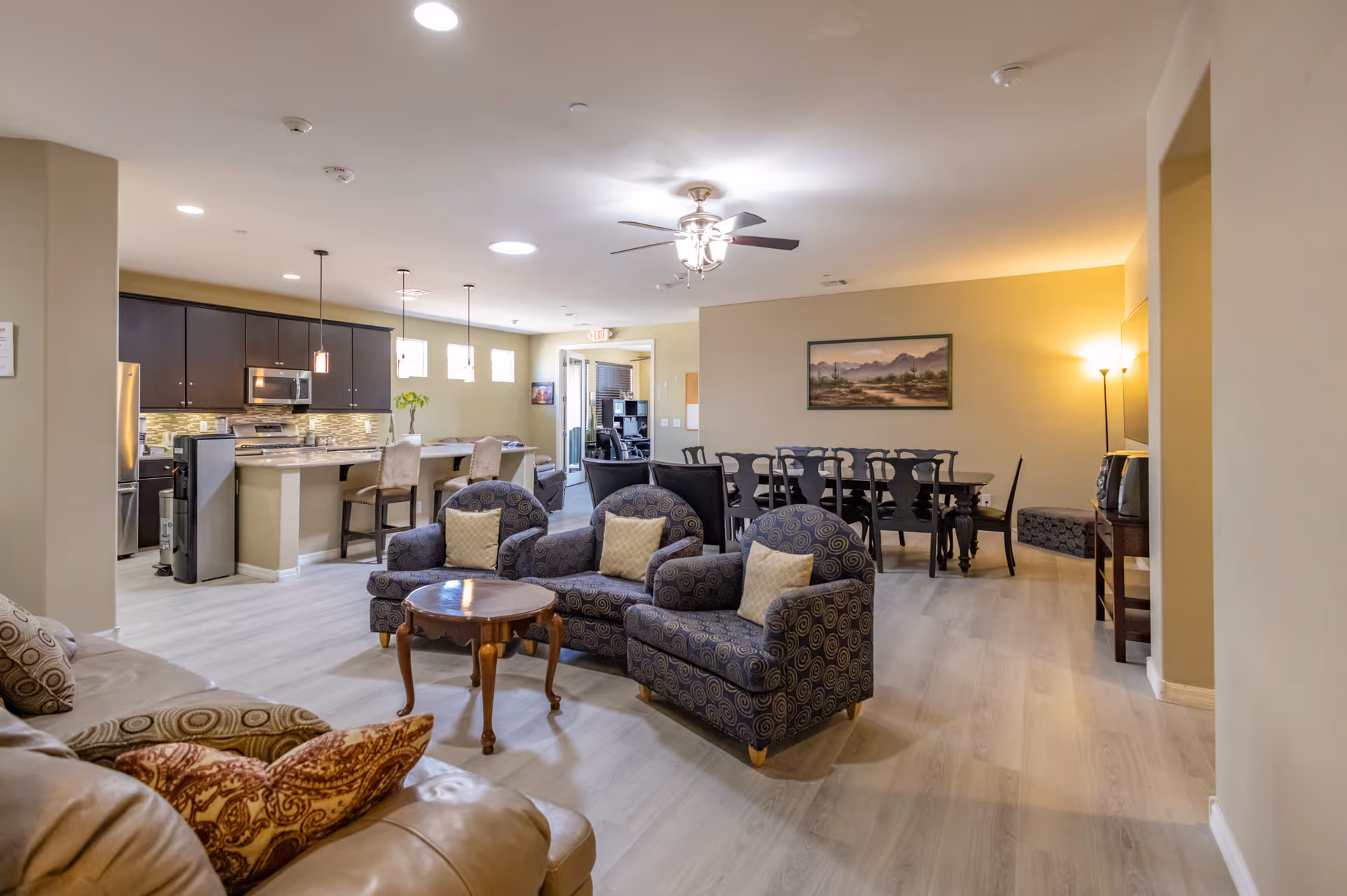 Open living area with kitchen island, seating, and dining table in a senior care facility.