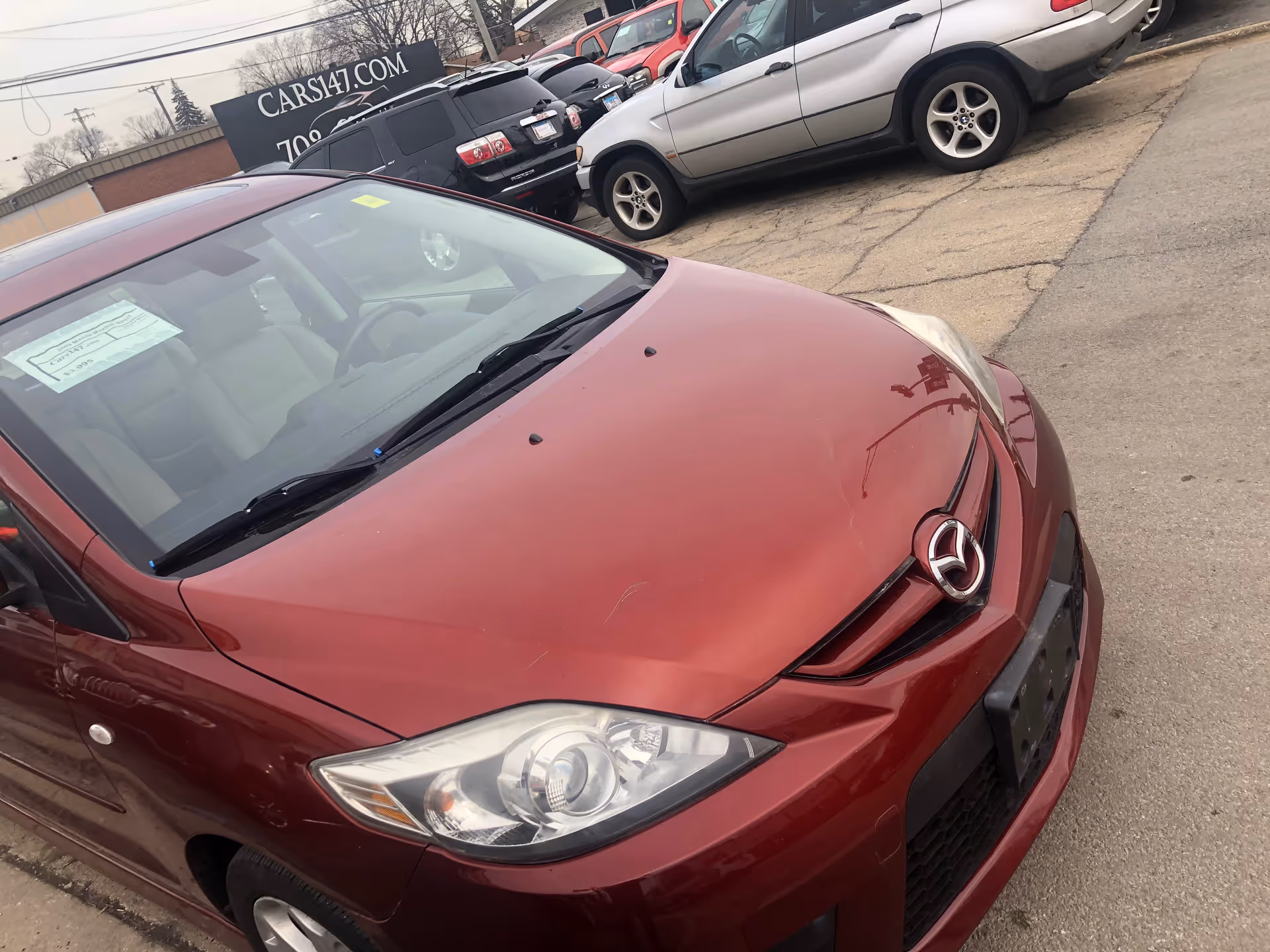 Red car parked in a lot beside a CARS147.COM sign.