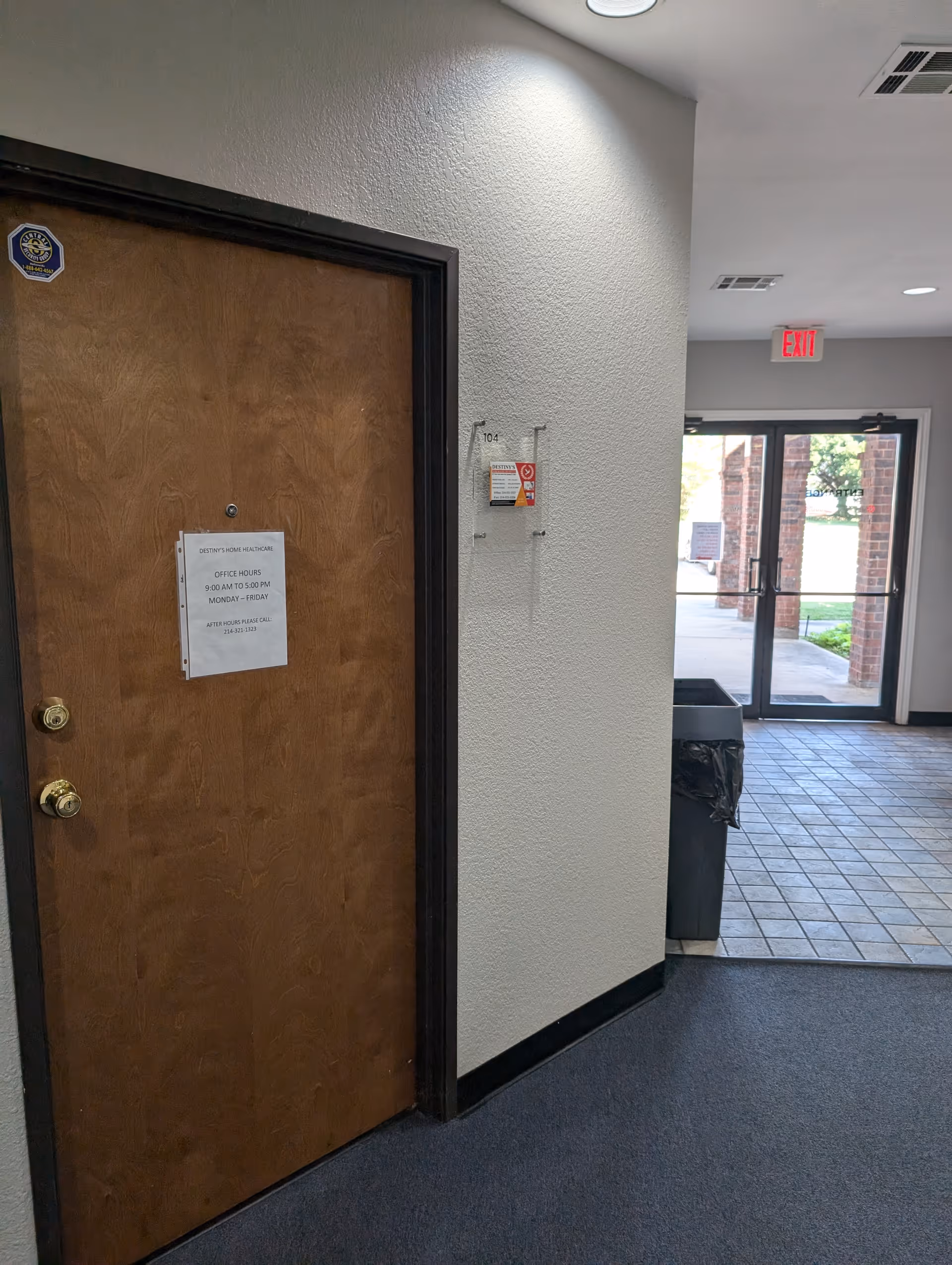 Interior hallway with wooden door, exit doorway, and trash can near tiled lobby.