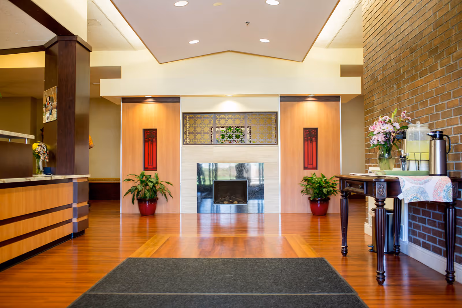Senior living facility lobby with wood floors, fireplace, plants, and a refreshment table.