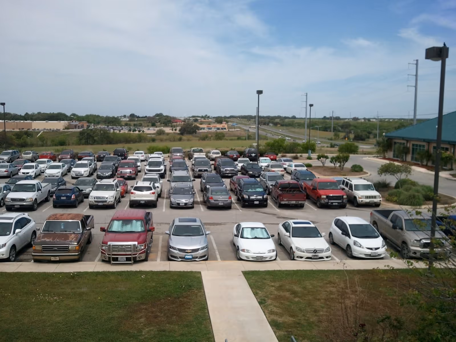 Wide parking lot filled with cars in front of a building with a teal roof.