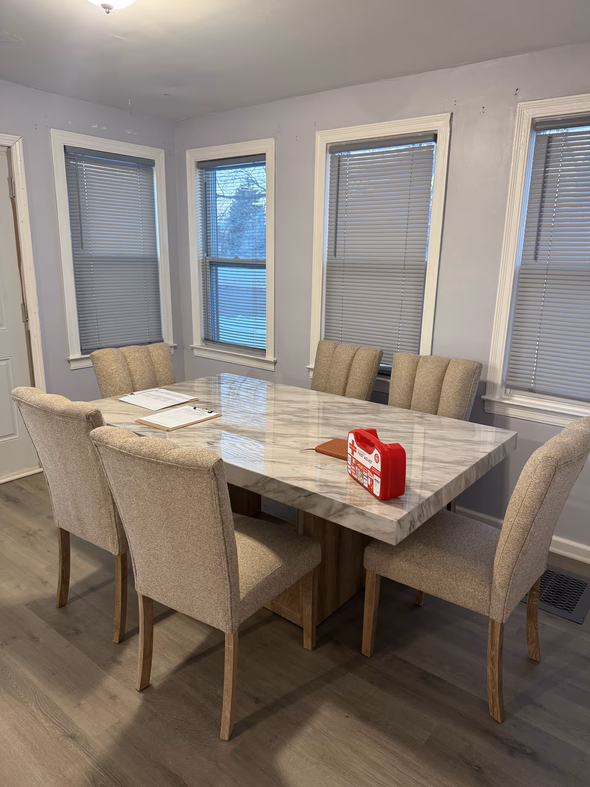 A marble dining table surrounded by beige upholstered chairs in a sunlit dining room.