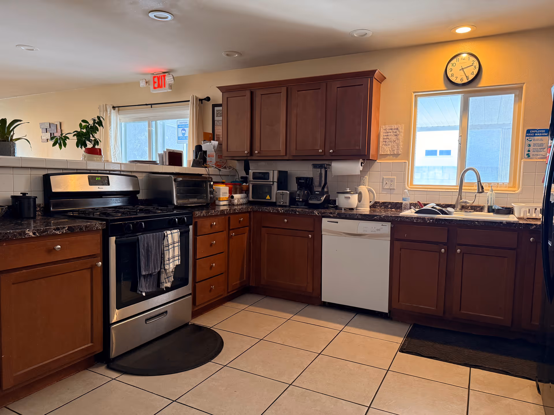 A spacious kitchen with dark wood cabinets, stainless stove and dishwasher, and sink by a window.
