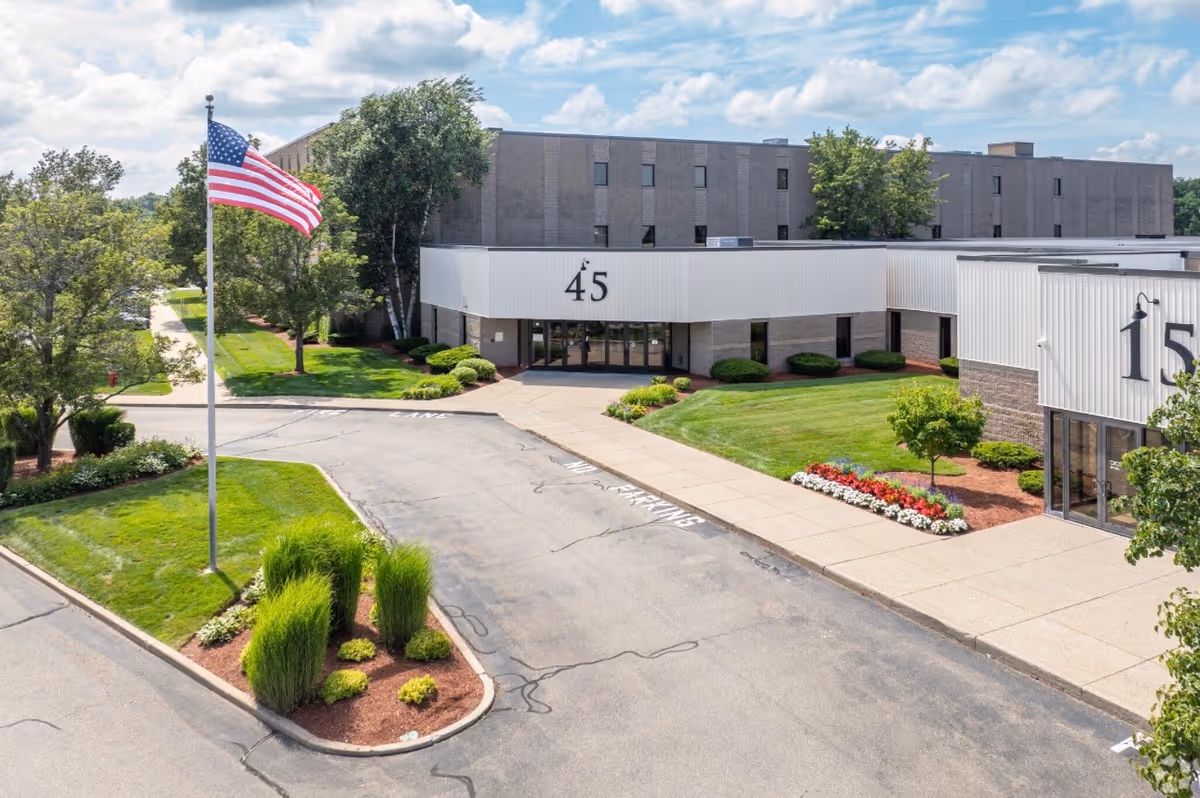 A front view of Abraham Comfort Care facility with the entrance and flag, surrounded by landscaping.