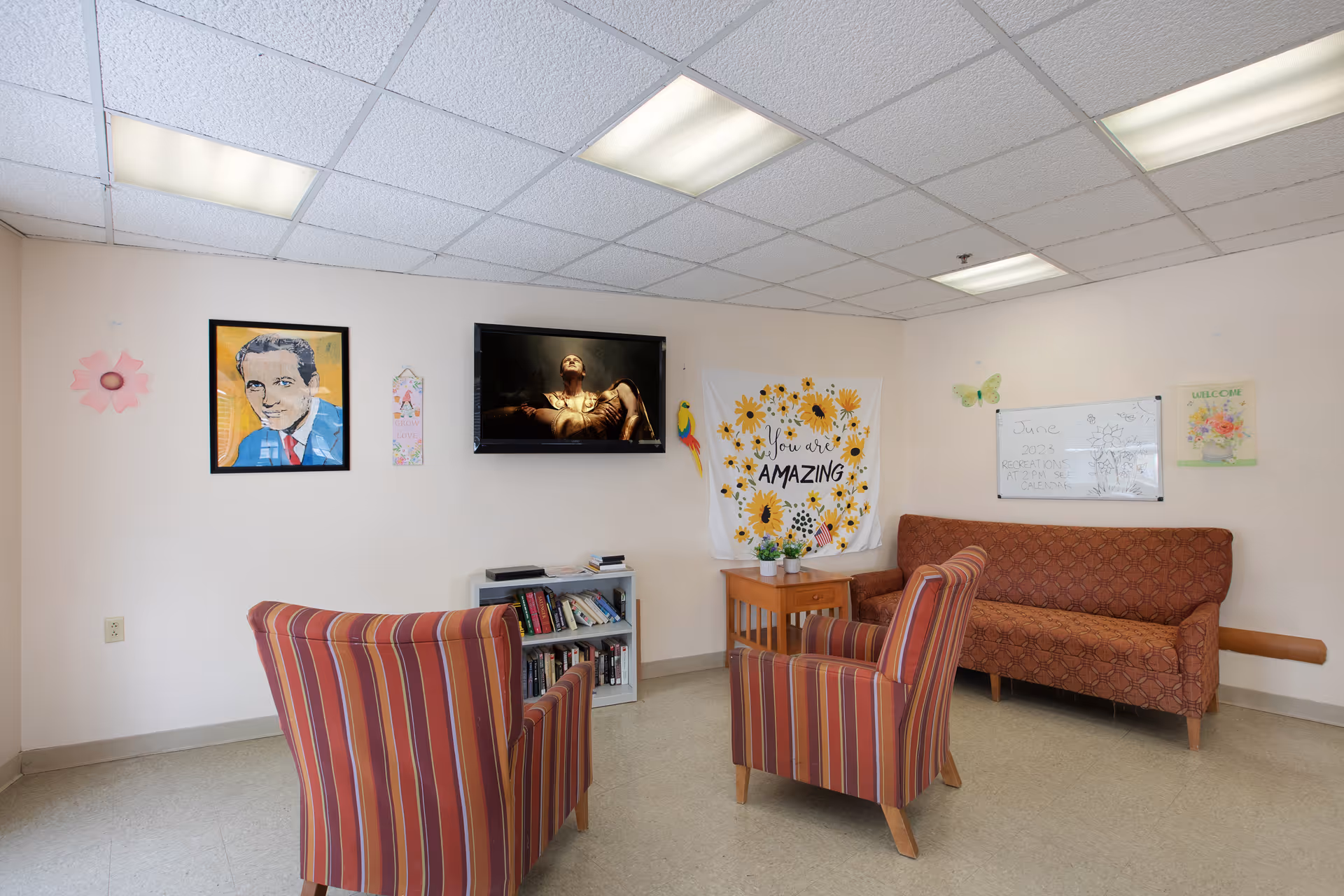 Cozy resident lounge with striped chairs, a sofa, television, bookshelf, and decorative wall art.