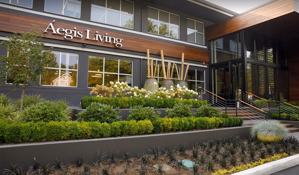 Exterior view of Aegis Living entrance with landscaped steps and large glass doors.