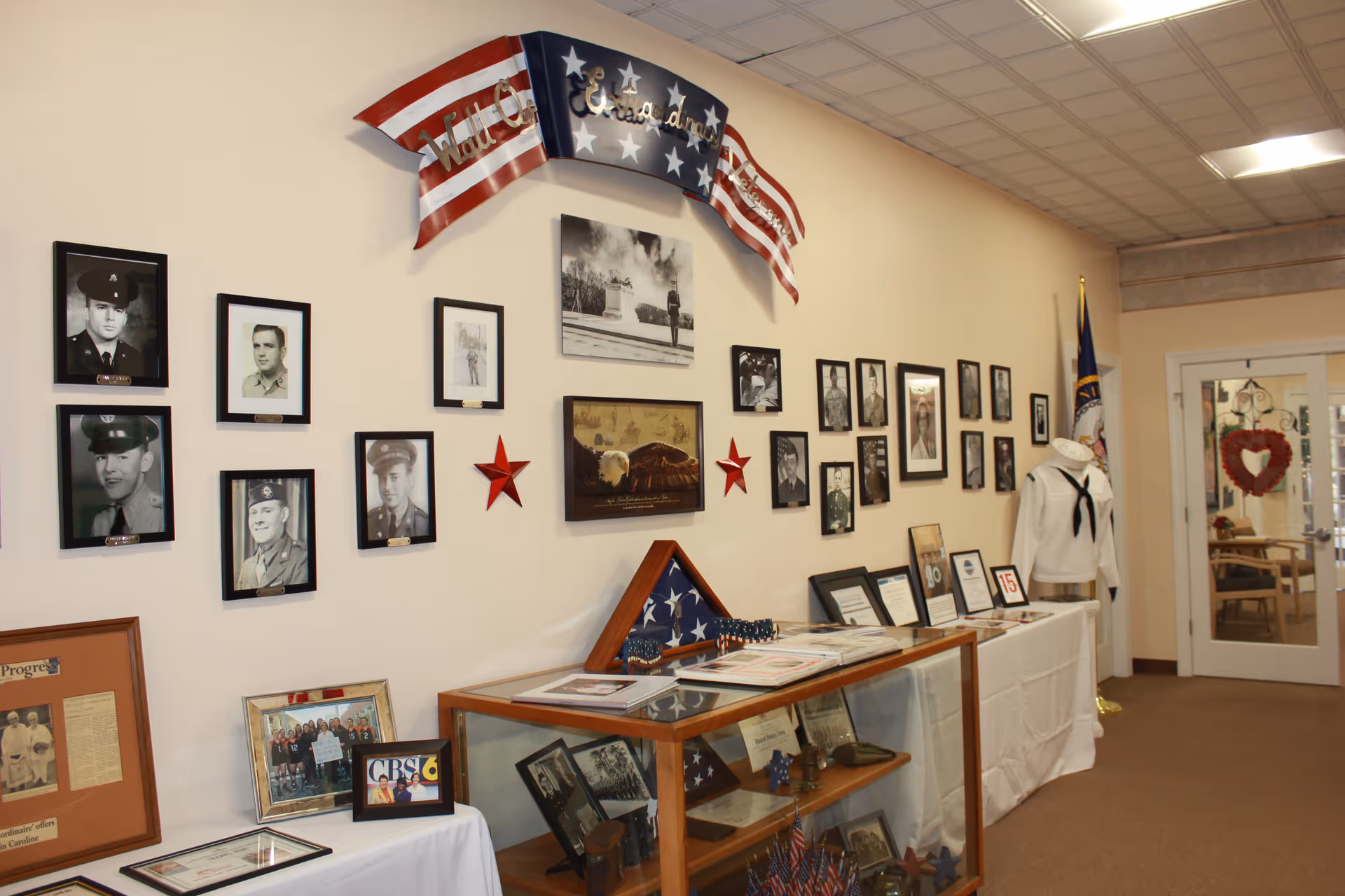 Interior hallway display with framed military photos, American flag decorations, and a glass display case.