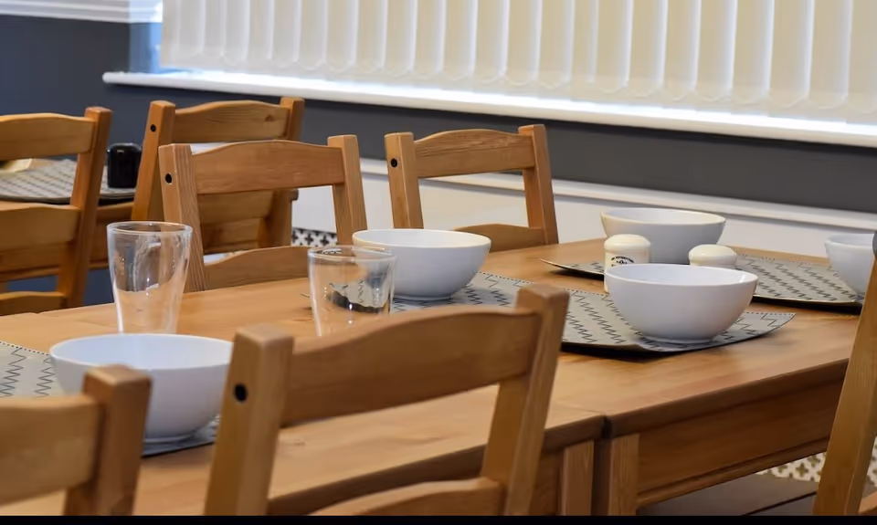 Wooden dining table set with bowls, glasses, and placemats in a bright dining area.