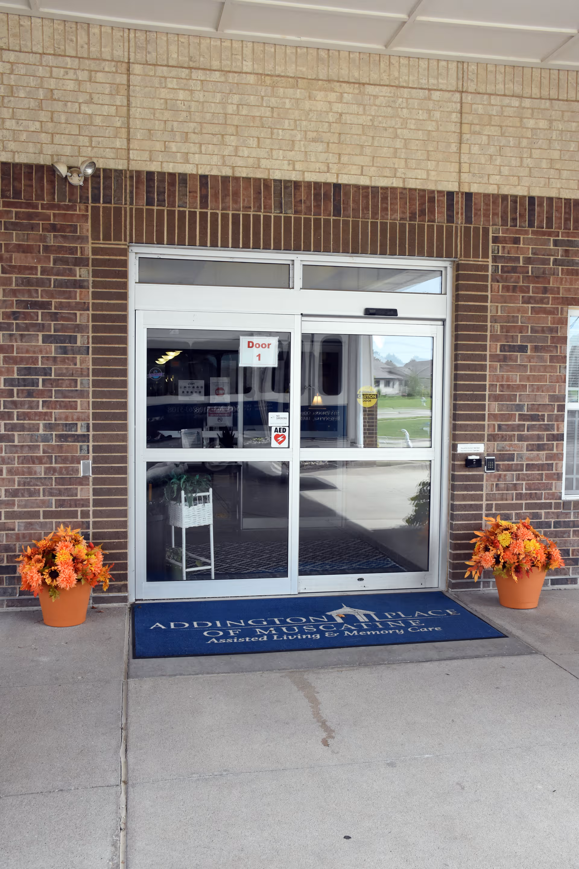 Front entrance of Addington Place of Muscatine, glass doors, brick exterior, orange fall flowers.