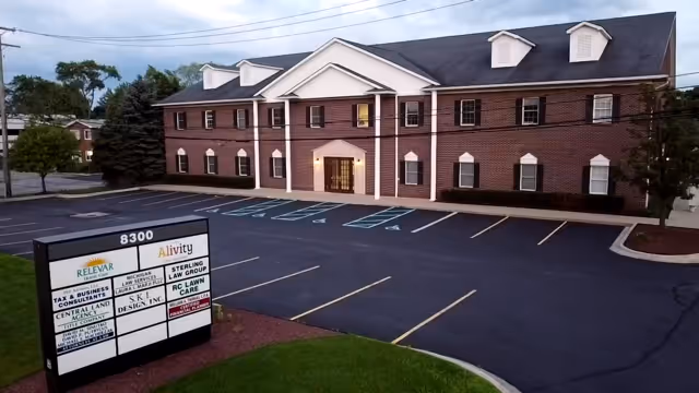 Brick senior living facility with a central front entrance, adjacent parking lot, and a facility sign.