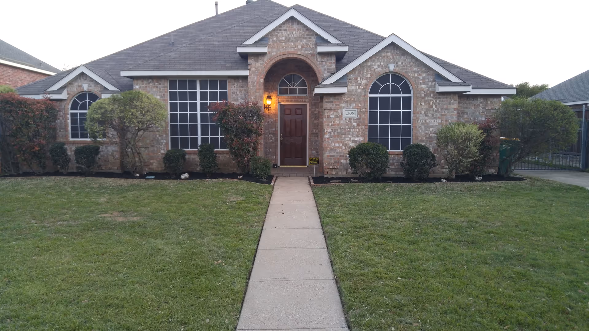 Brick facade with arched windows, a central front door, and a walkway leading to the entrance.