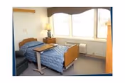 A single bedroom with blue bedding, a nightstand, and a large window.
