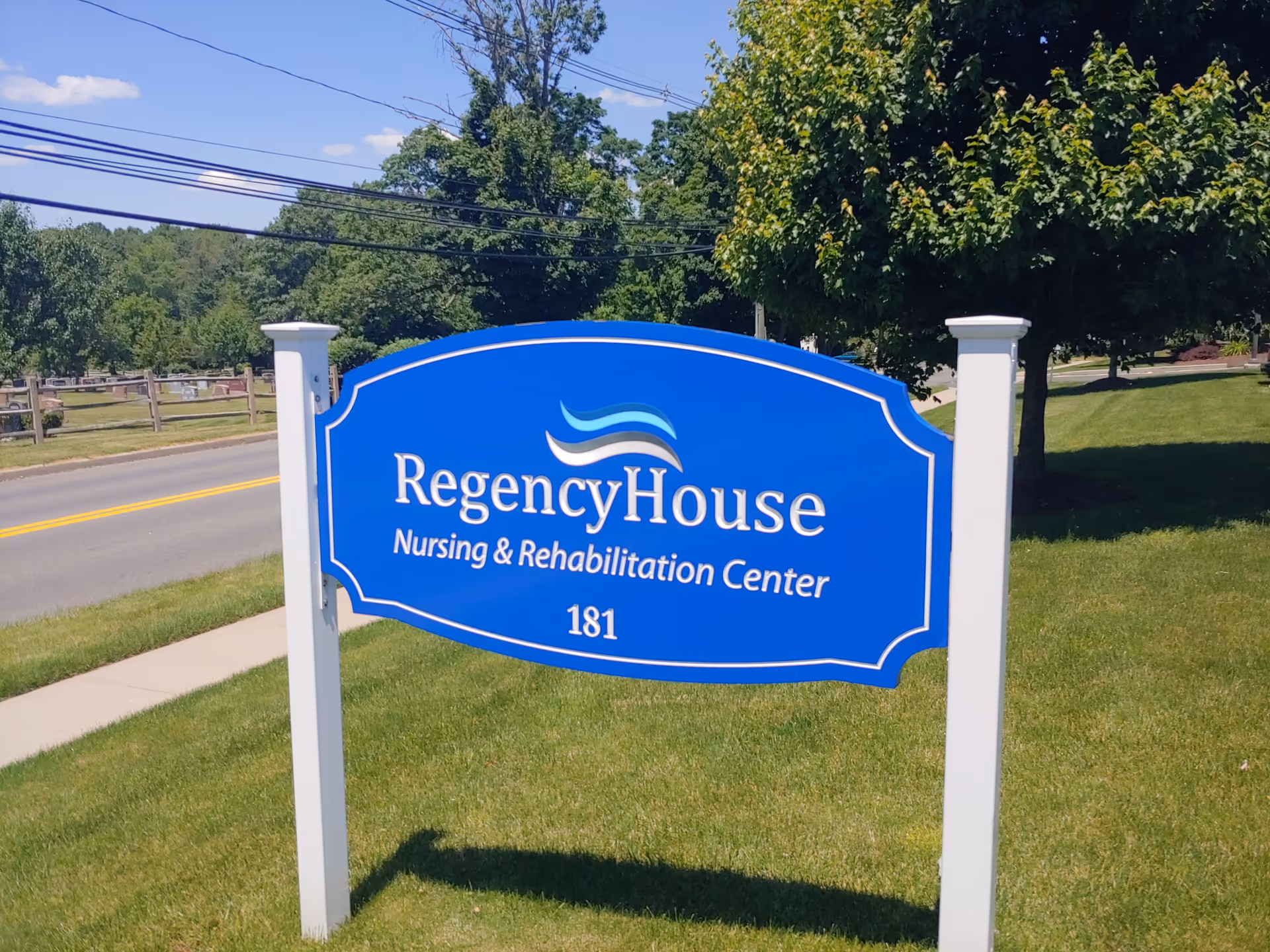 Blue Regency House sign on a grassy lawn by the road.