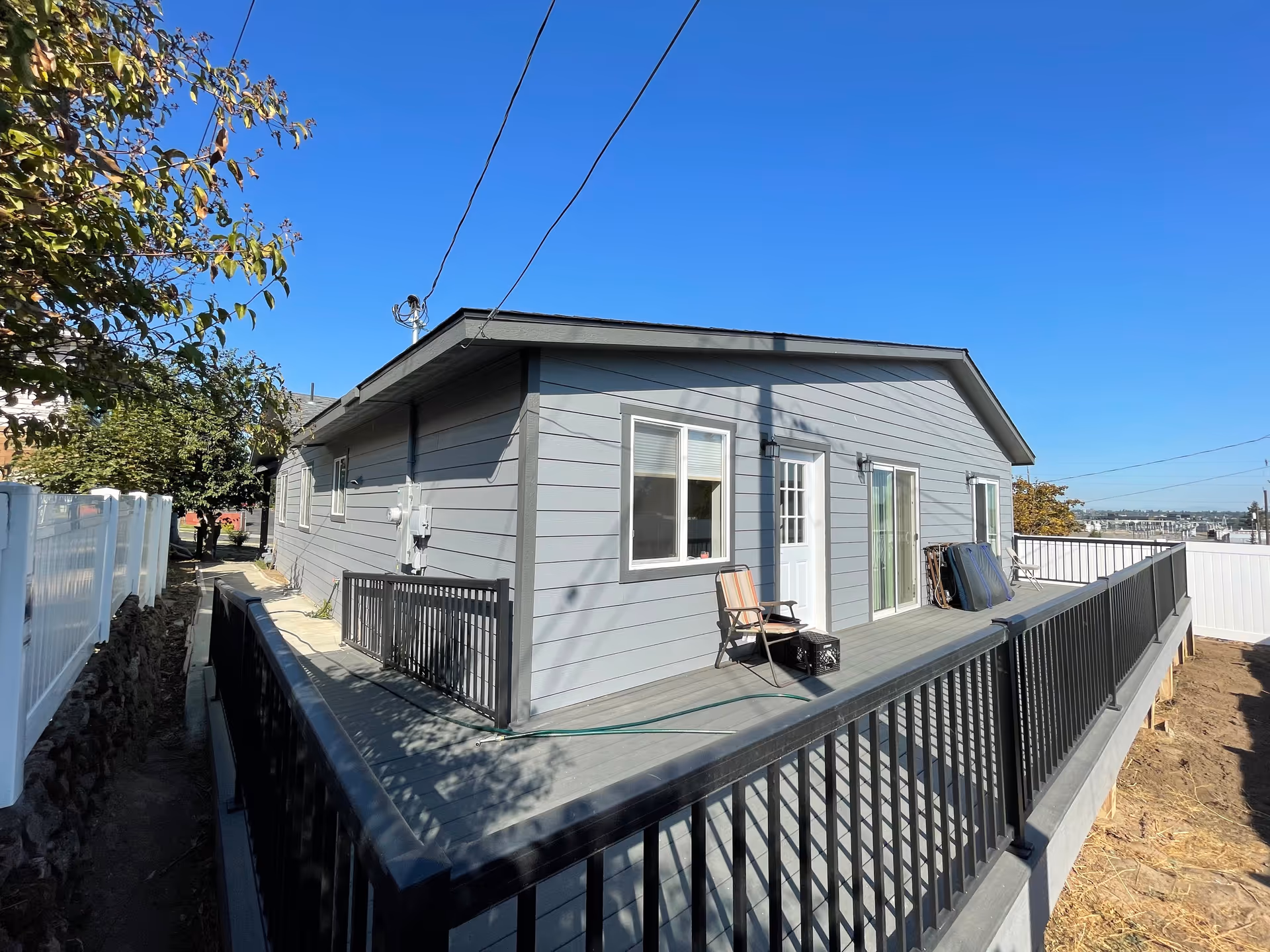 Gray single-story house with a wooden deck and black railing under clear blue sky.