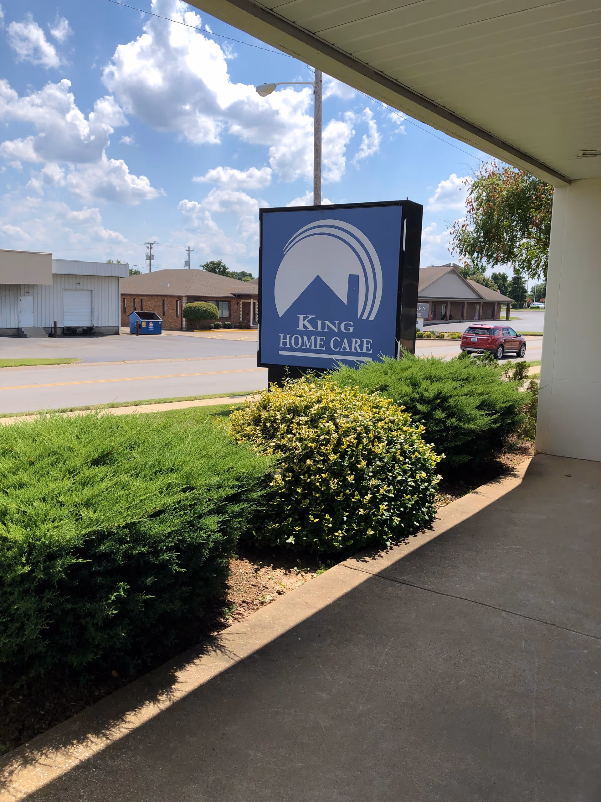 Exterior view of King Home Care sign with shrubs and a street in front.