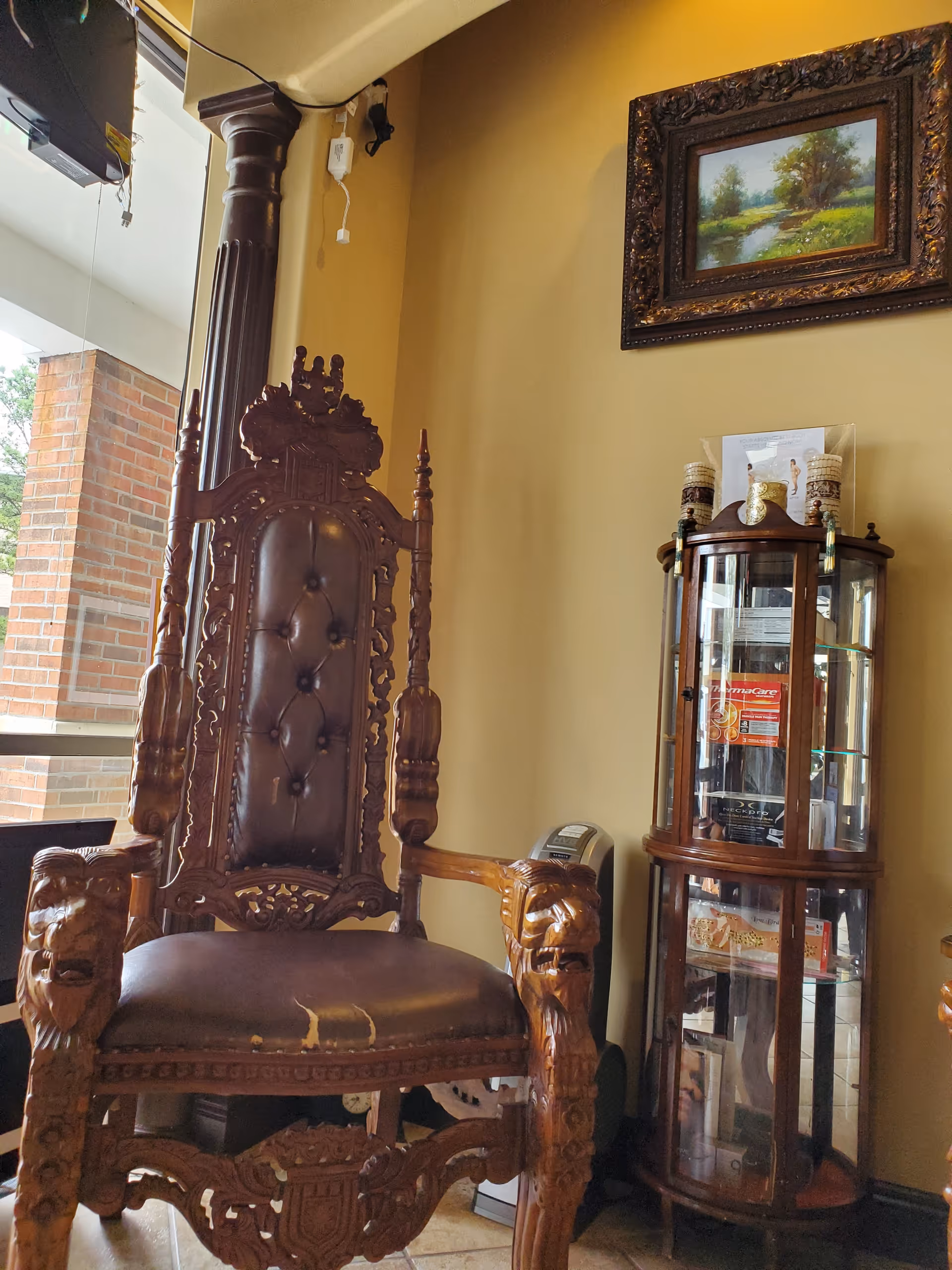 Luxurious carved wooden throne chair beside curved glass cabinet in a warm interior.