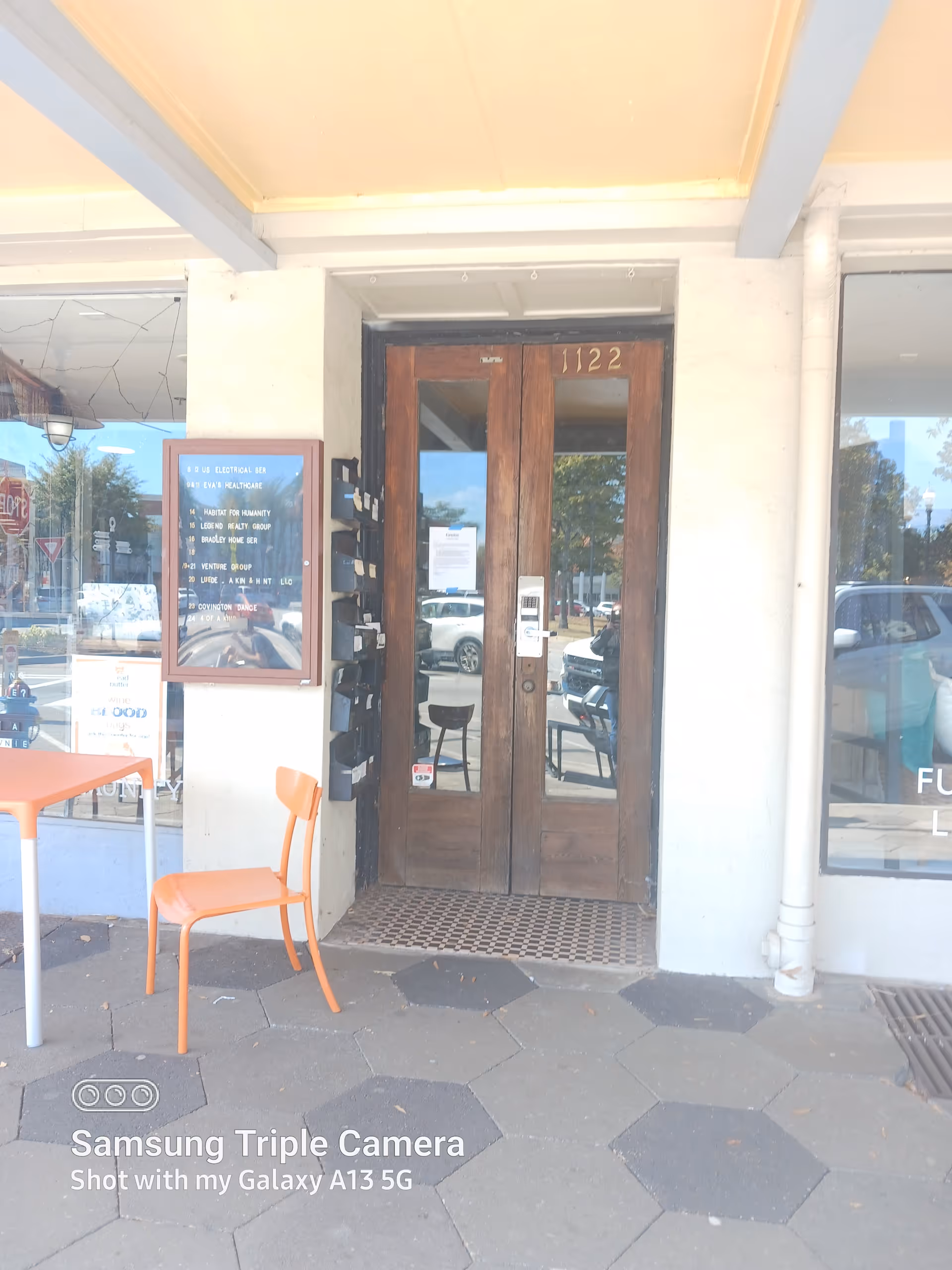 Wooden front door with glass panels labeled 1122, orange chair and table outside storefront