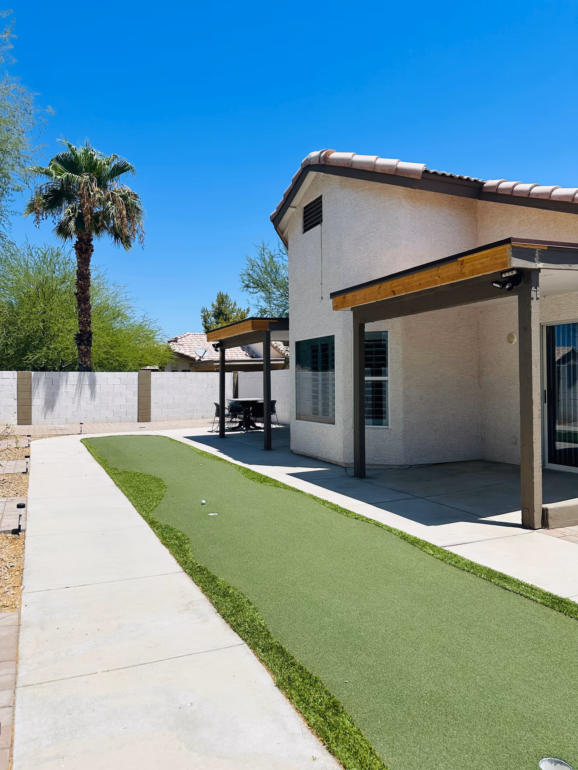 Exterior view of a beige building with a covered patio and artificial green putting area.