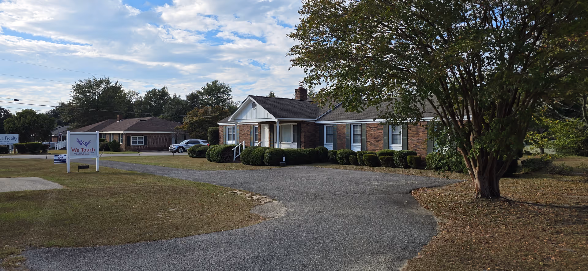 Brick, single-story senior care facility with a curved driveway and a We-Touch sign at left.