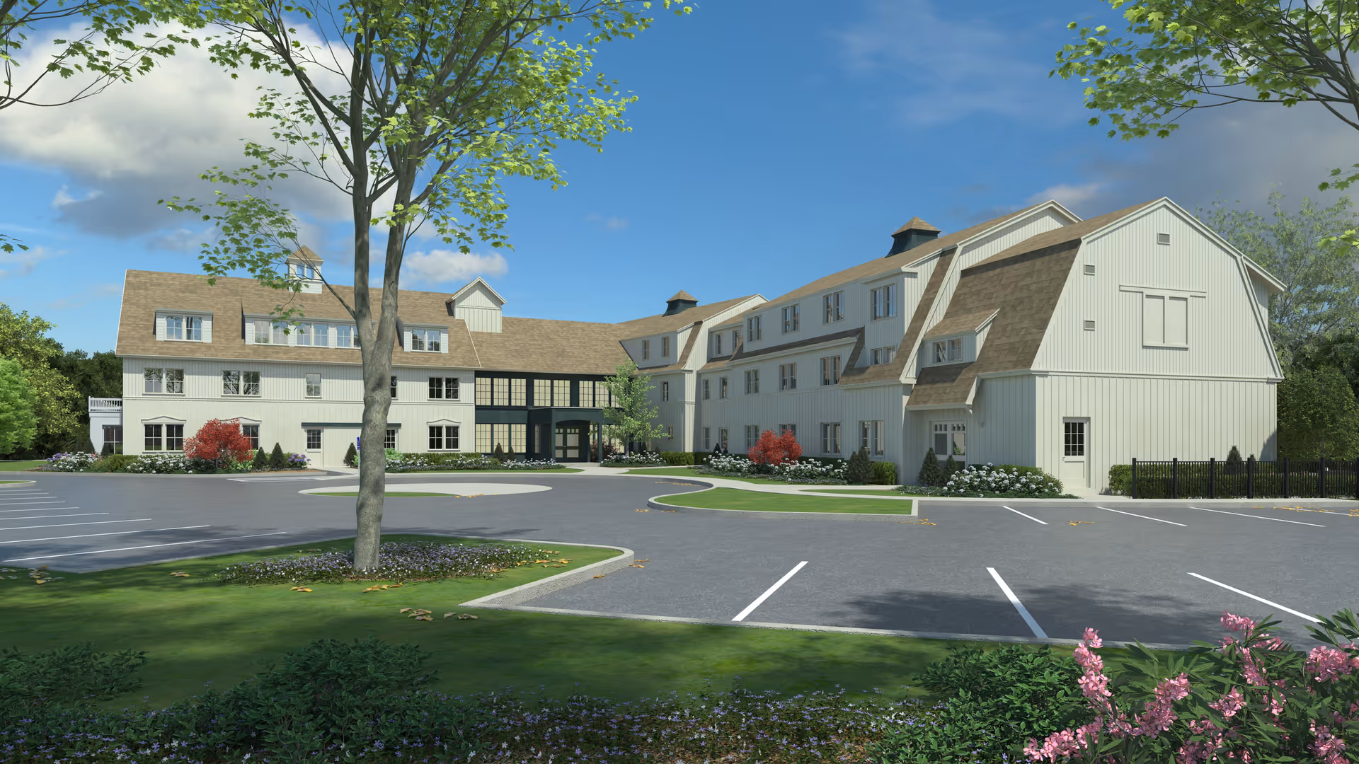 Exterior view of a large, multi-story assisted living facility with beige siding and brown roofs, surrounded by landscaped greenery, trees, and a parking lot under a partly cloudy blue sky.