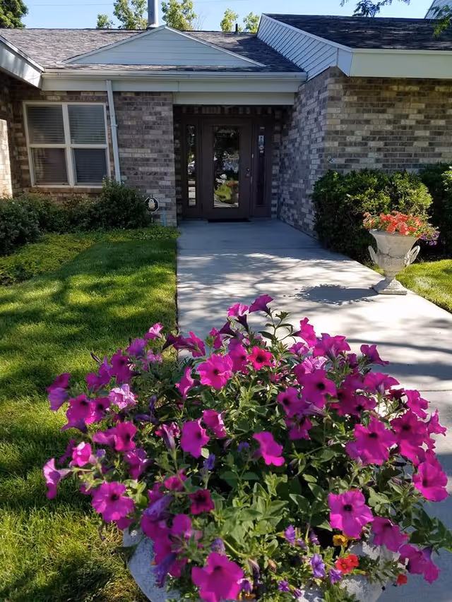 Brick senior living facility exterior entrance with a concrete walkway and pink flowers
