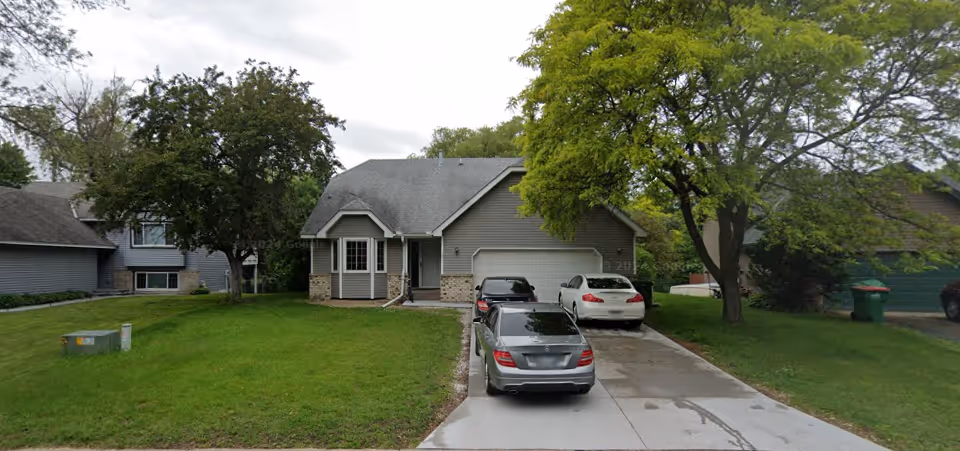 Residential-style senior living facility exterior with a driveway and parked cars.