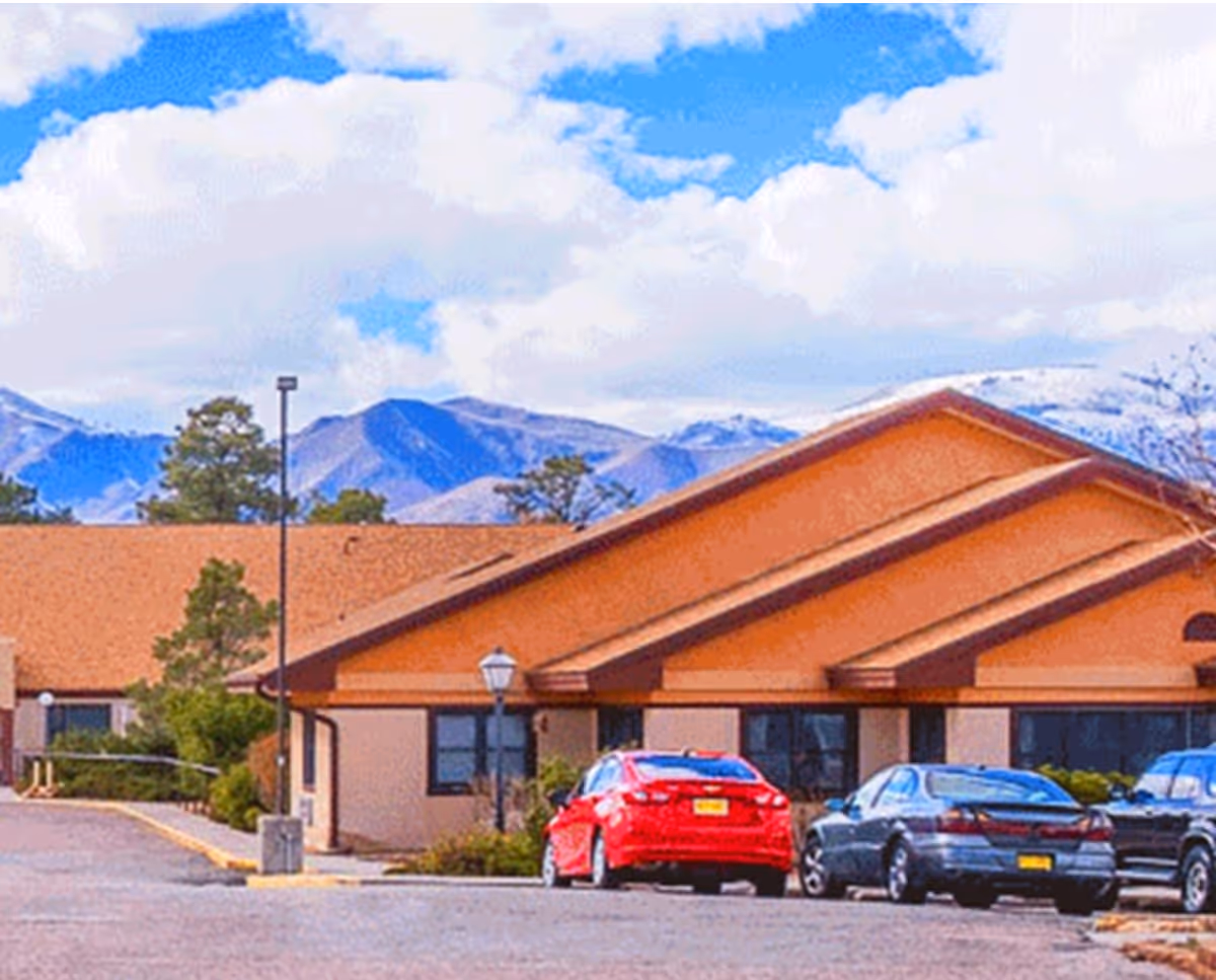 A single-story nursing center exterior with a brown roof and parked cars in front.