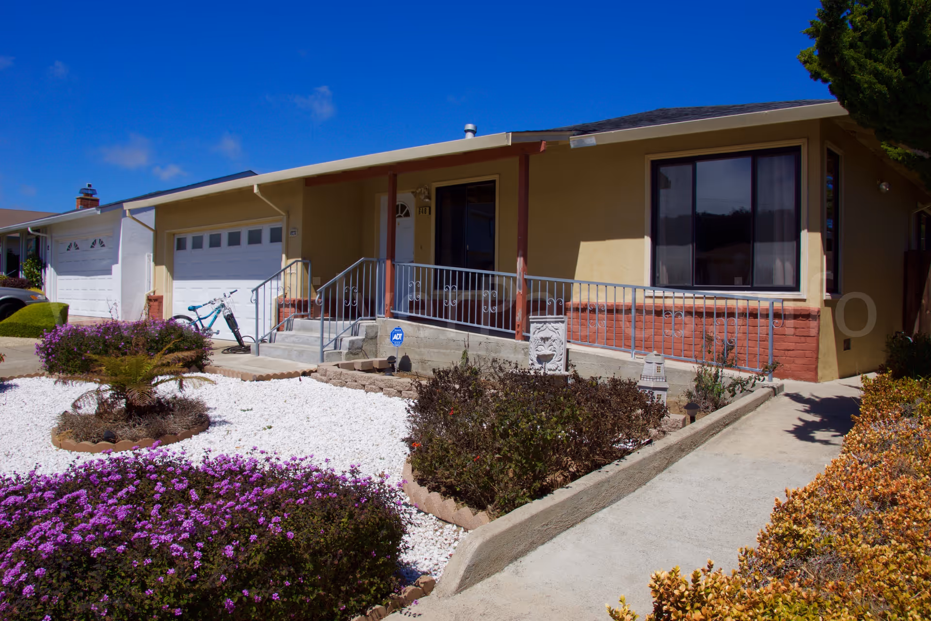 Front view of a single-story beige senior living home with a porch and landscaped yard.