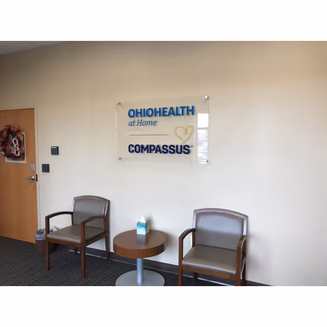 Interior lobby area with two chairs, a round table, and a wall sign OhioHealth Compassus.