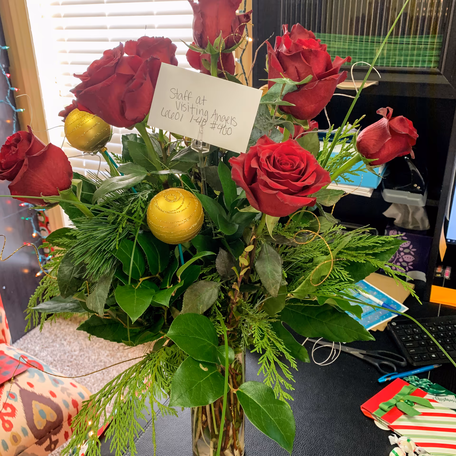 Bouquet of red roses and greenery on a desk with office supplies indoors.