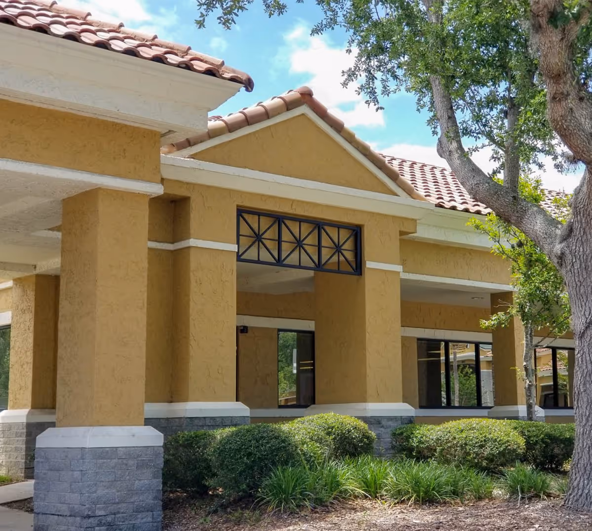 Exterior view of Brooks Rehabilitation Home Health facility with tan stucco walls and red tile roof.