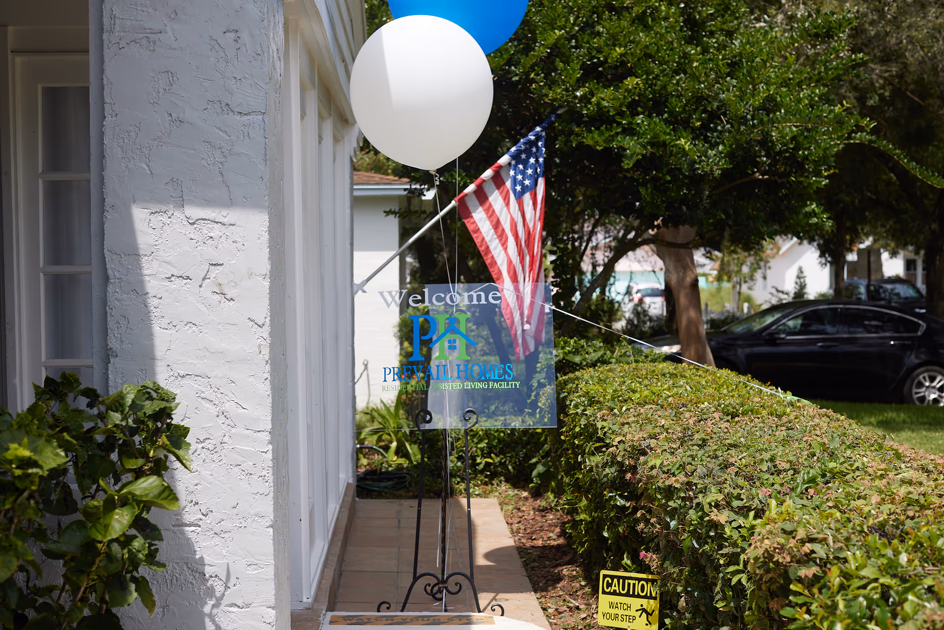 Exterior of a building entrance with a welcome sign, balloons, and an American flag.