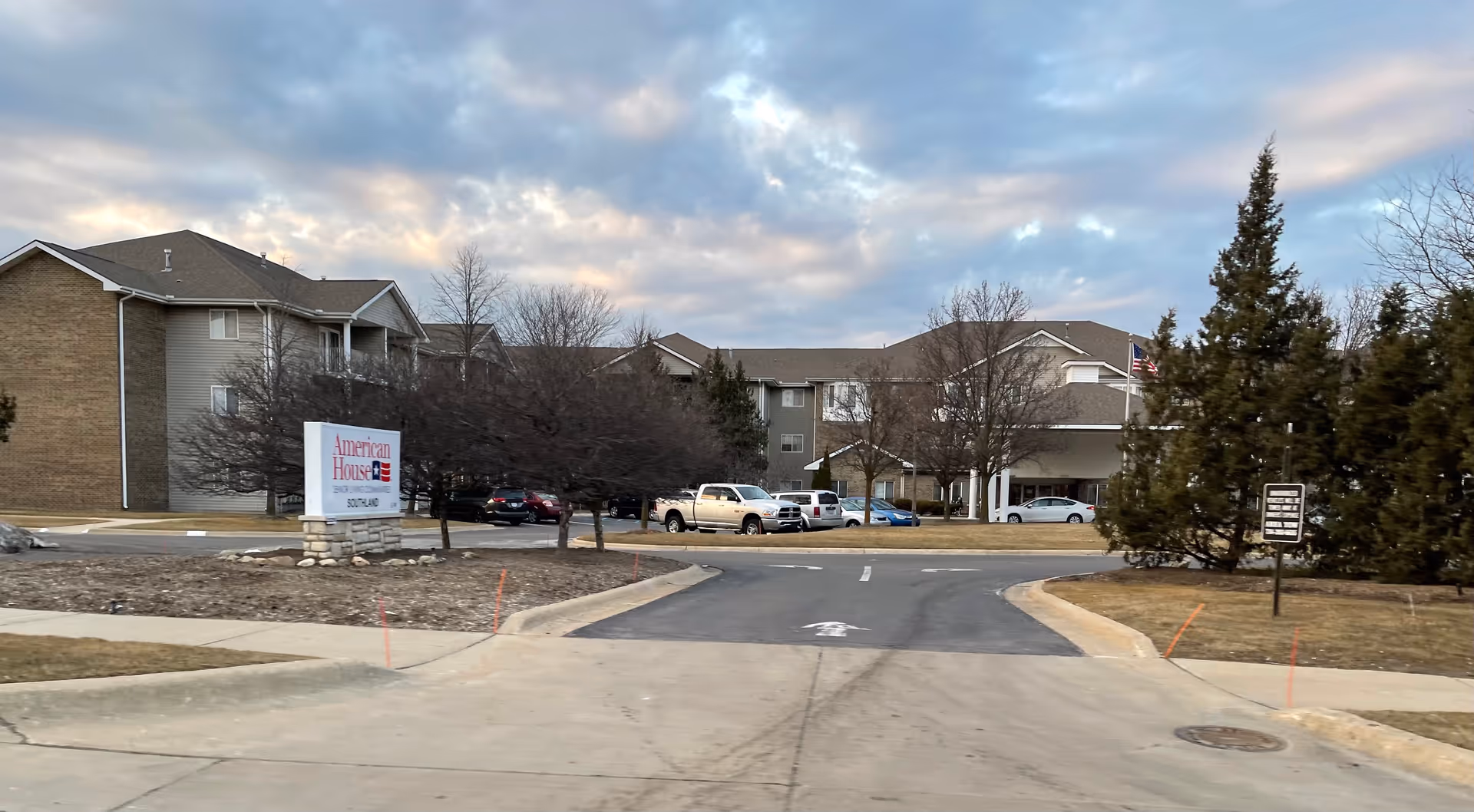 Exterior view of American House Southland senior living facility with sign and parked cars.