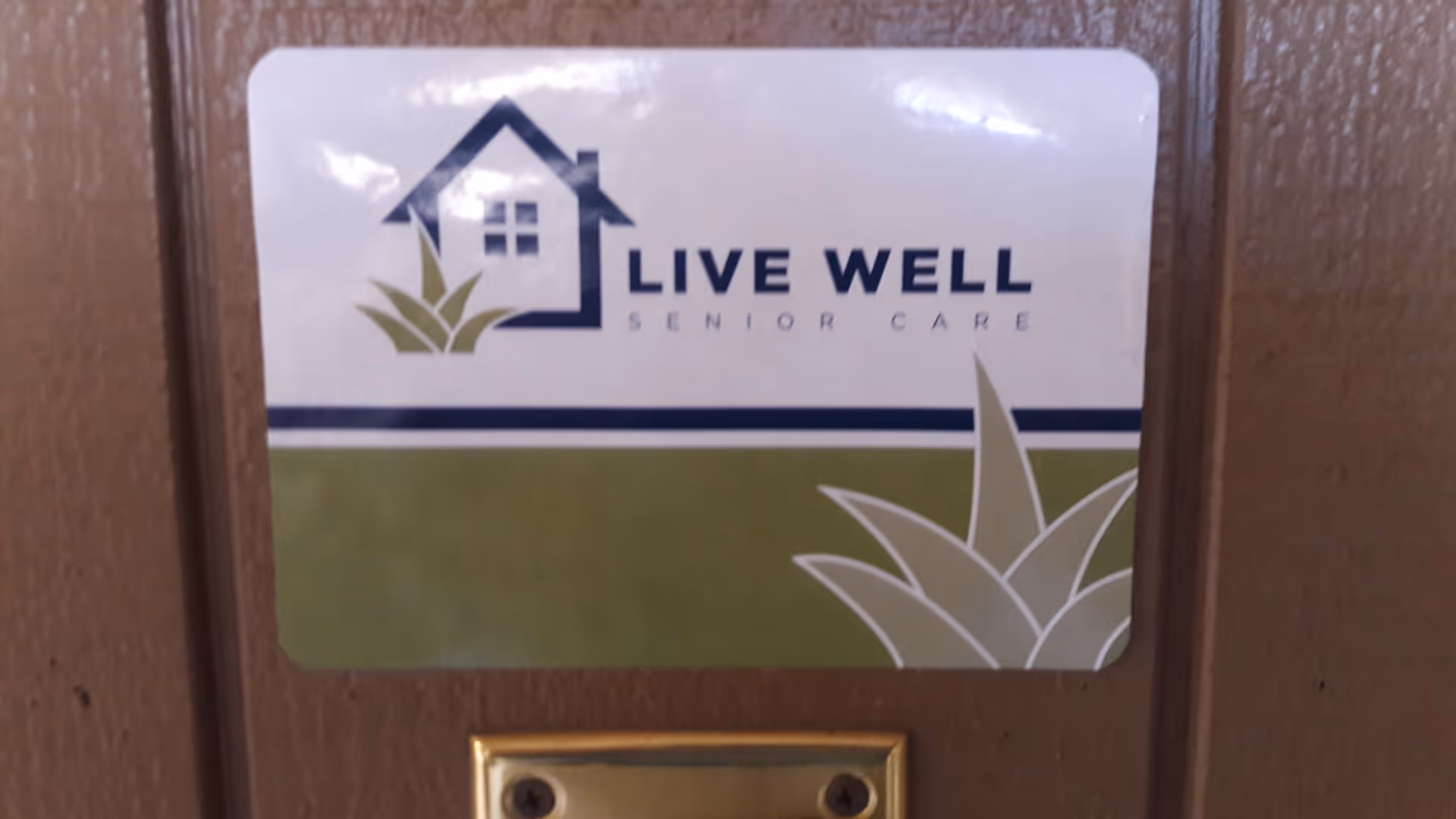 Sign reading Live Well Senior Care with house and plant logo mounted on wood door.