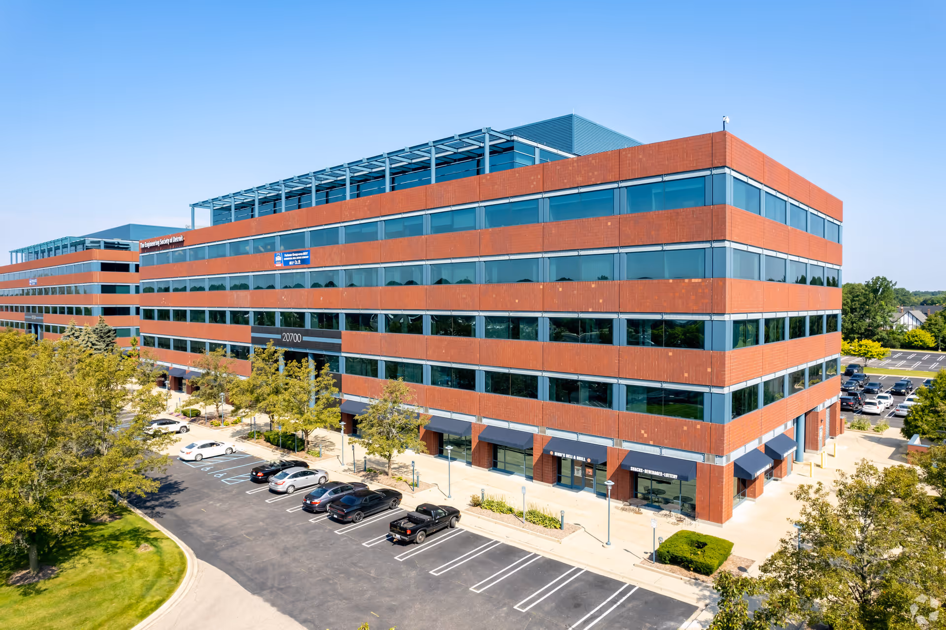 A large brick office building with glass windows, a parking lot, and surrounding trees.