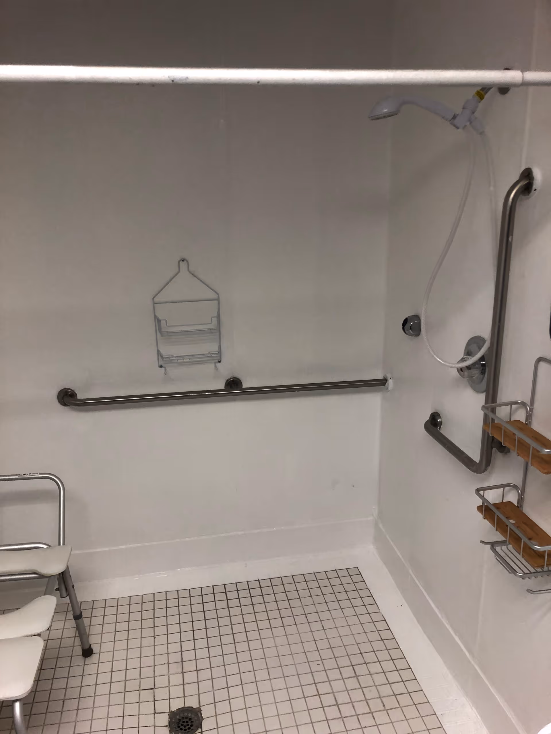Accessible shower room with grab bars, handheld shower, and a shower chair.