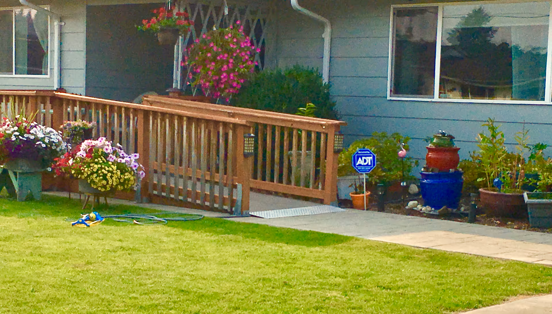 Front exterior of a home with a wooden ramp, hanging baskets, and potted plants.