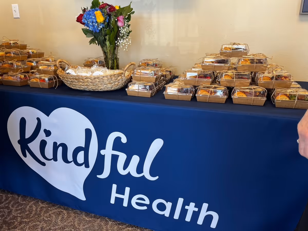 Indoor table display with wrapped gift baskets and a blue Kindful Health banner.
