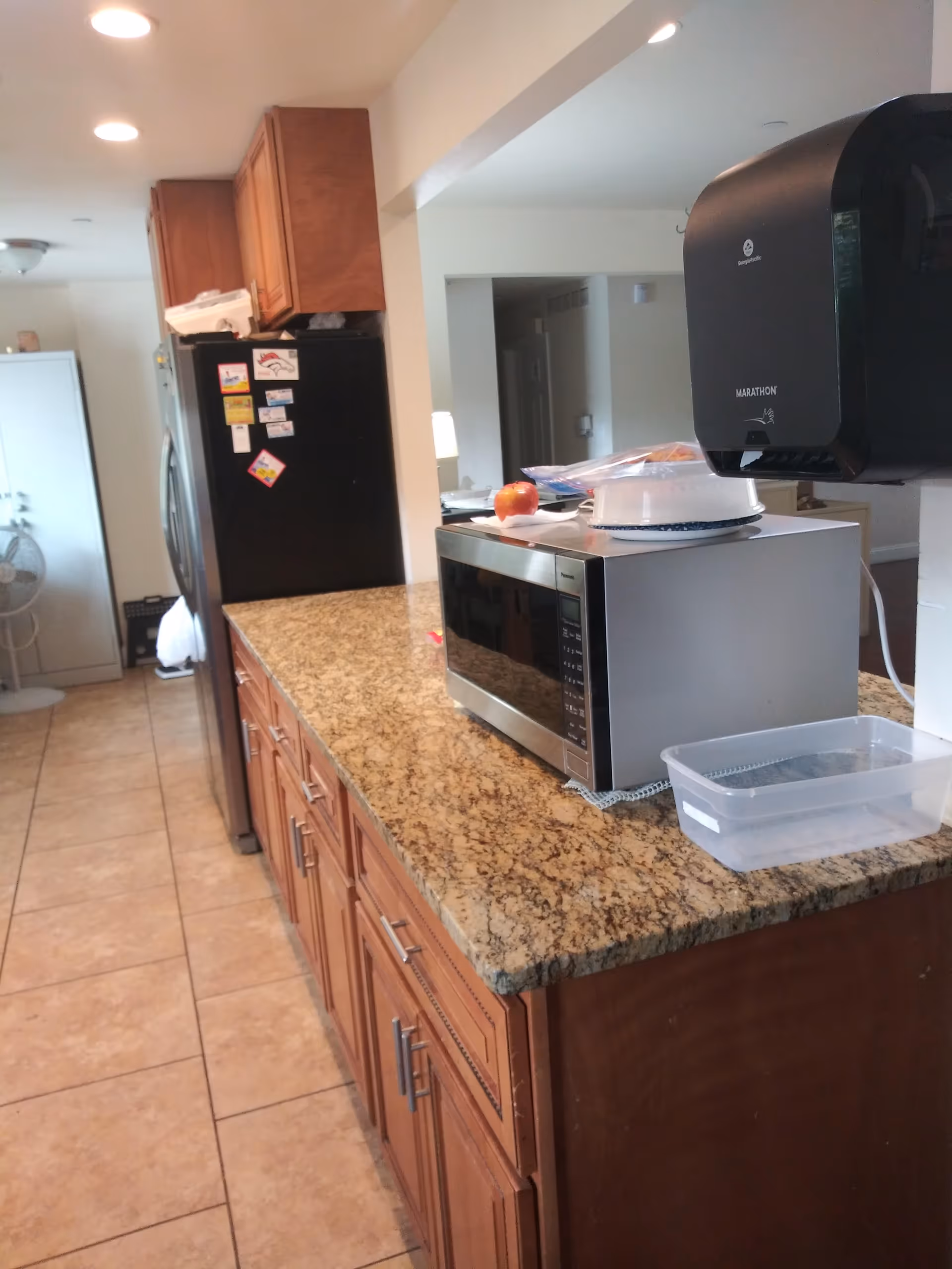 Kitchen counter with microwave, refrigerator, and granite countertop in a senior living facility.