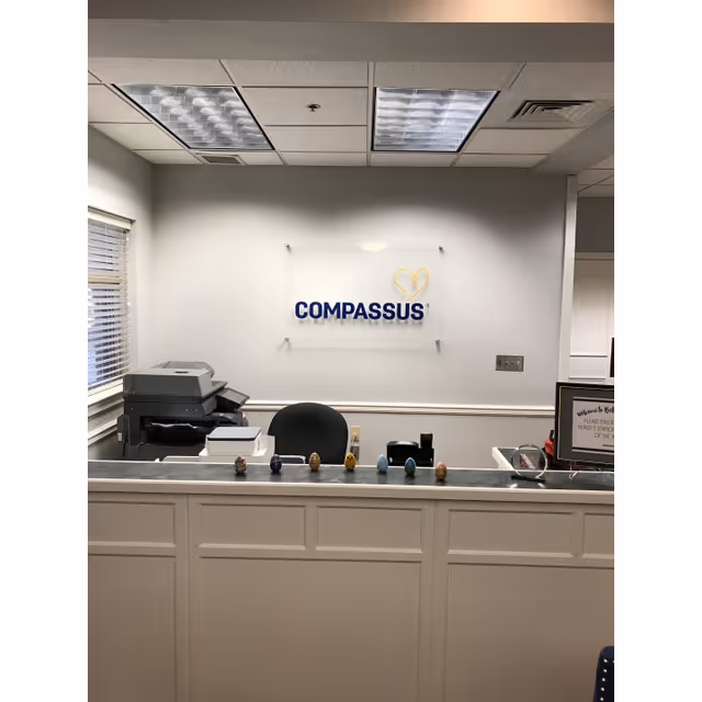 Reception desk in a Compassus lobby with a wall sign and office equipment.
