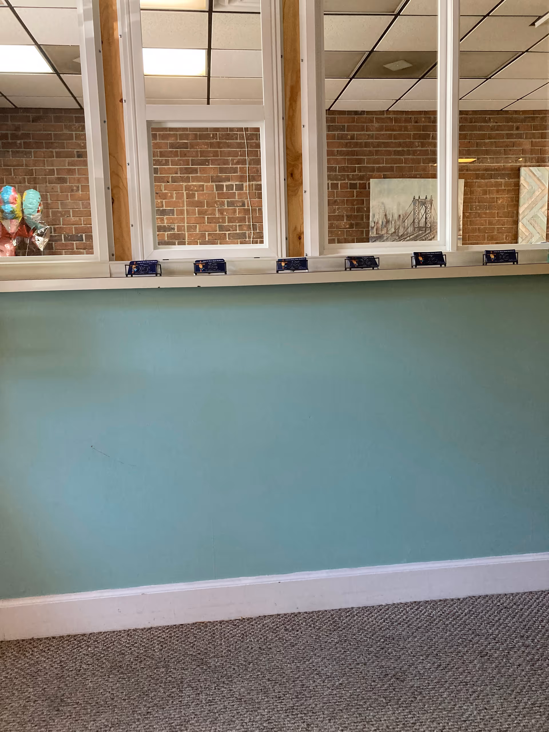 Teal wall with large windows, carpeted floor, and brick wall backdrop.