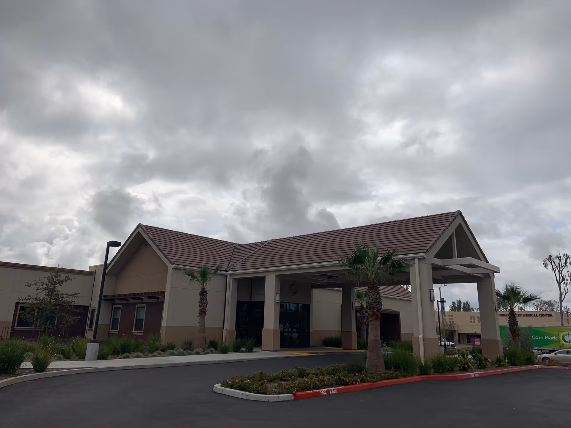 Exterior view of Trellis Chino senior living facility entrance with a covered drop-off and palms.