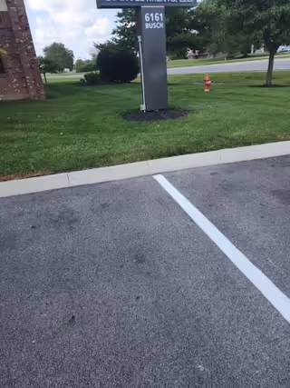 Parking lot beside a grassy area with a sign, hydrant, and trees in background.