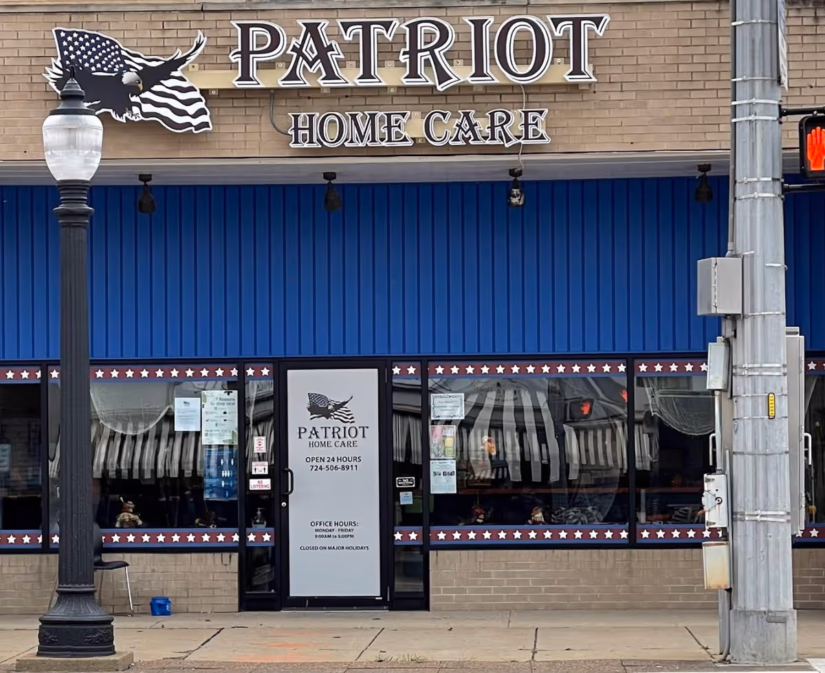 Blue storefront with Patriot Home Care sign, large windows, and a sidewalk in front.