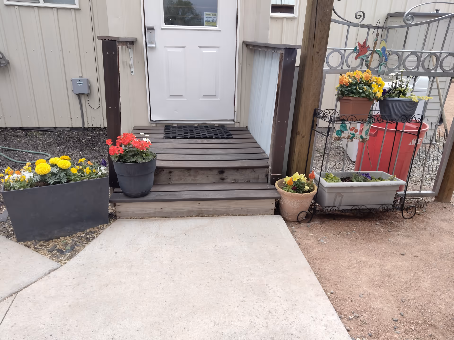 Front entrance to Delta House featuring wooden steps, a white door, and colorful potted flowers.