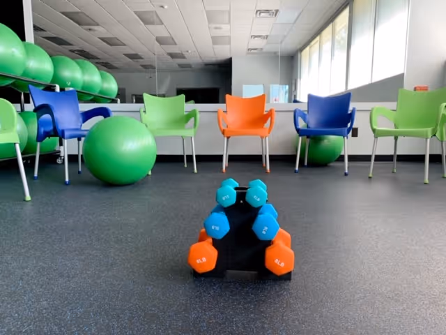 Interior exercise room with colorful chairs, large stability balls, and stacked dumbbells.